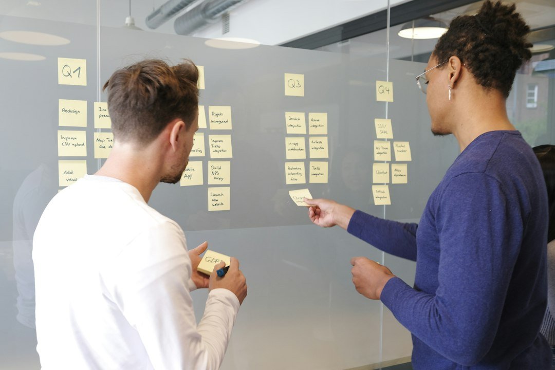 Two people collaborating on a project plan using yellow sticky notes on a glass wall